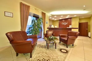 A hotel reception area with leather chairs, a reception desk, and a large window with curtains. - Vingis (Marijampole)