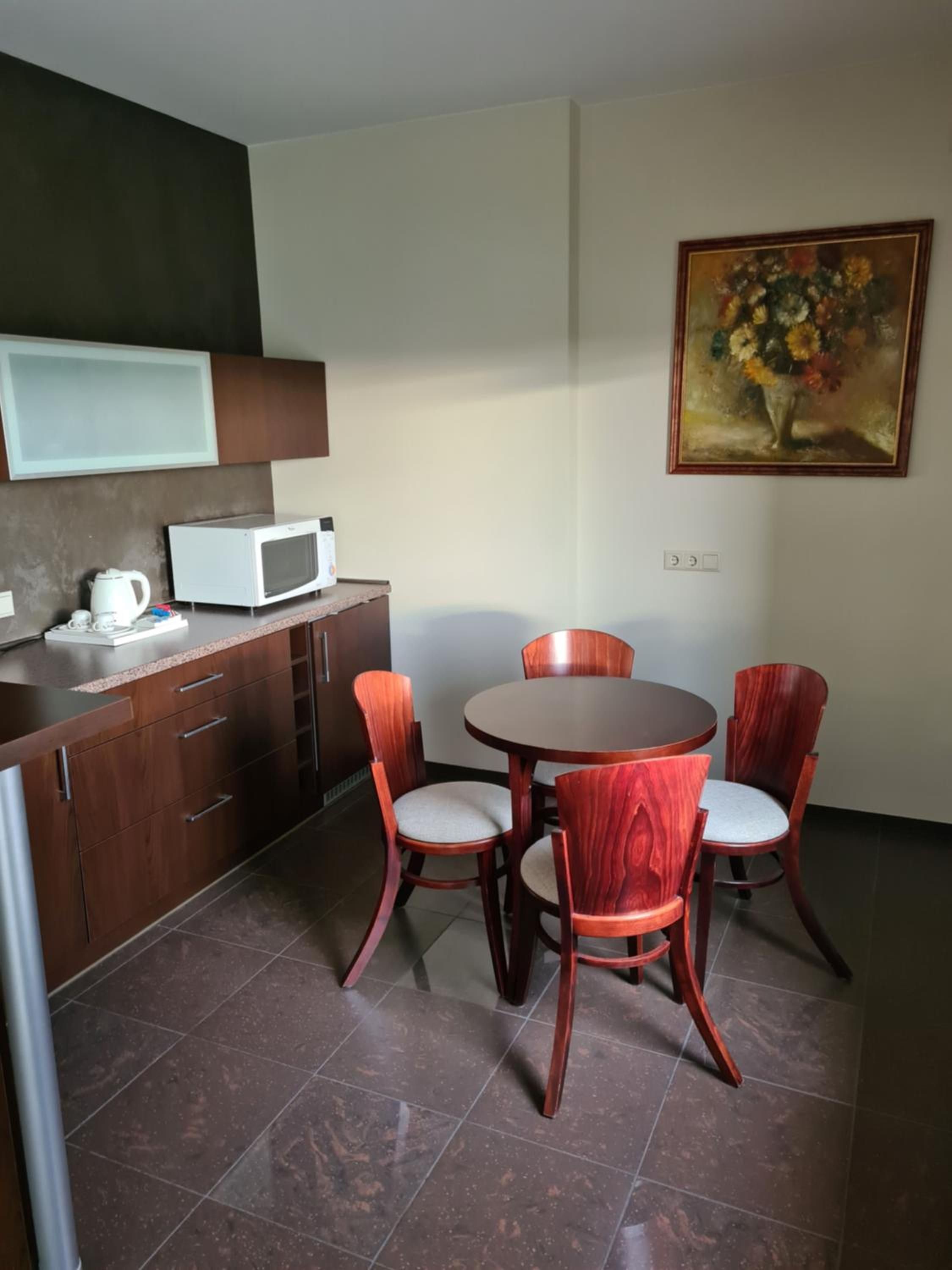 A compact kitchen with a microwave, a kettle, and a dining table with four chairs.