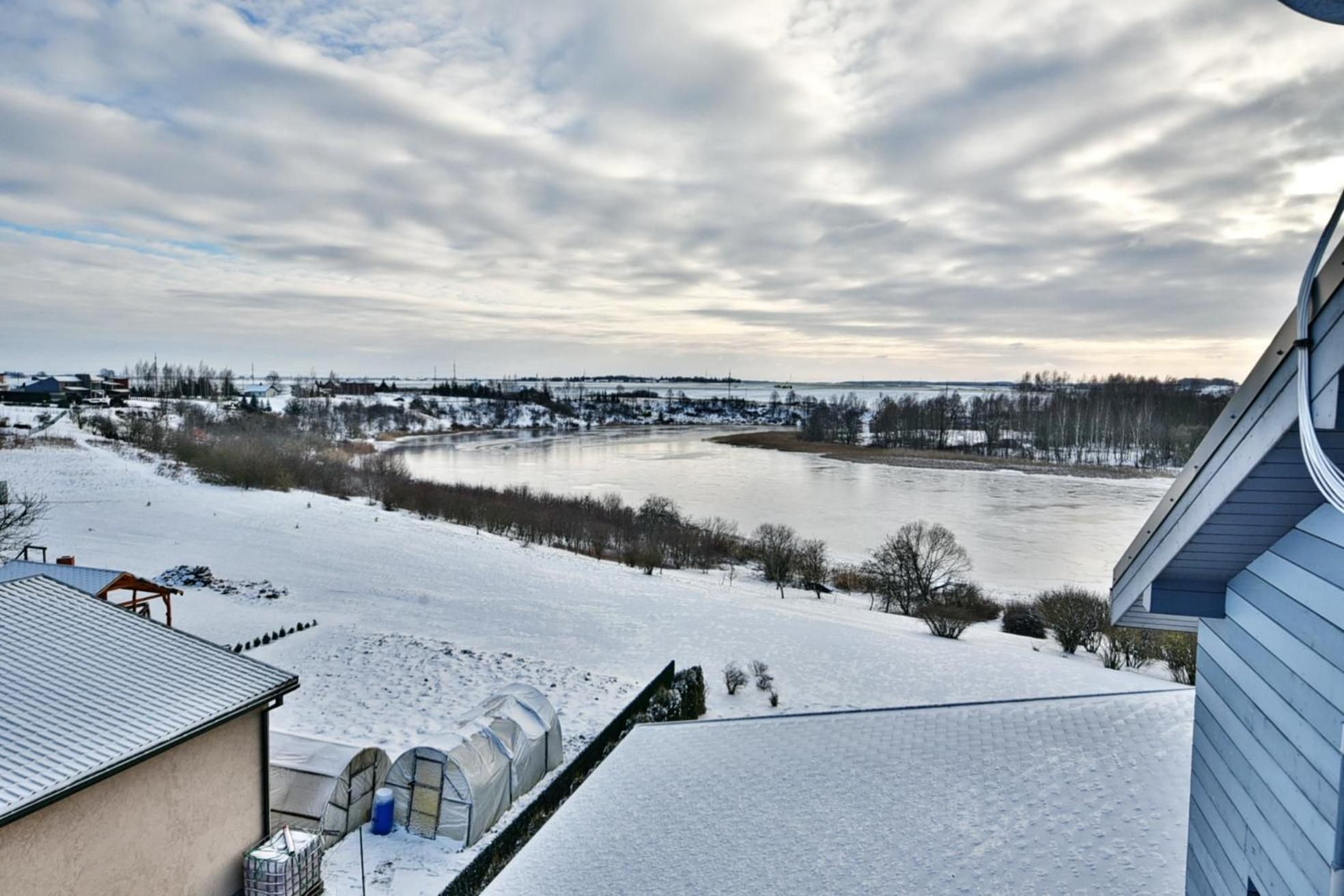 A snow-covered landscape with a river, buildings, and a clear sky.