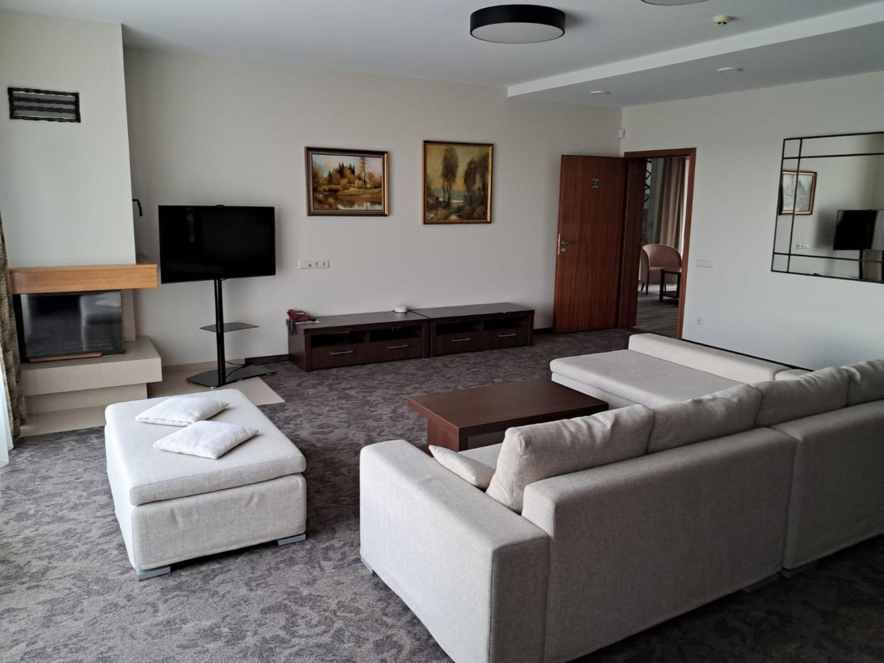A modern living room with a sofa set, a flat-screen TV, a wooden cabinet, and two paintings on the wall.