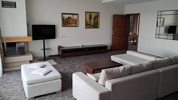 A modern living room with a sofa set, a flat-screen TV, a wooden cabinet, and two paintings on the wall.