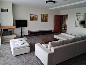 A modern living room with a sofa set, a flat-screen TV, a wooden cabinet, and two paintings on the wall.