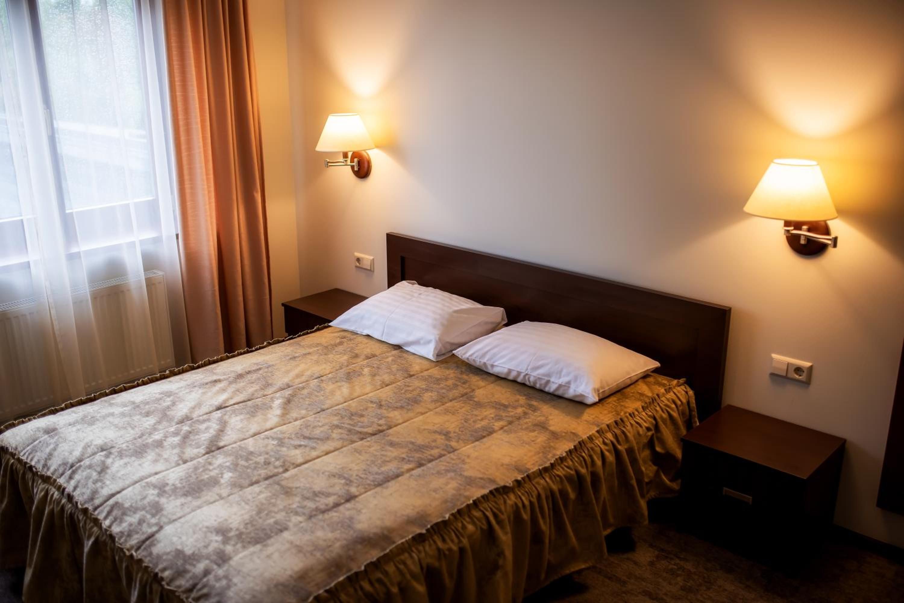 Een hotelkamer met een bed, twee bedlampen, een raam met gordijnen en een radiator.