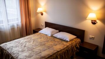Een hotelkamer met een bed, twee bedlampen, een raam met gordijnen en een radiator.