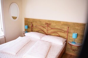 Uma cama bem arrumada com cabeceira de madeira, duas luminárias de cabeceira e um espelho redondo na parede.