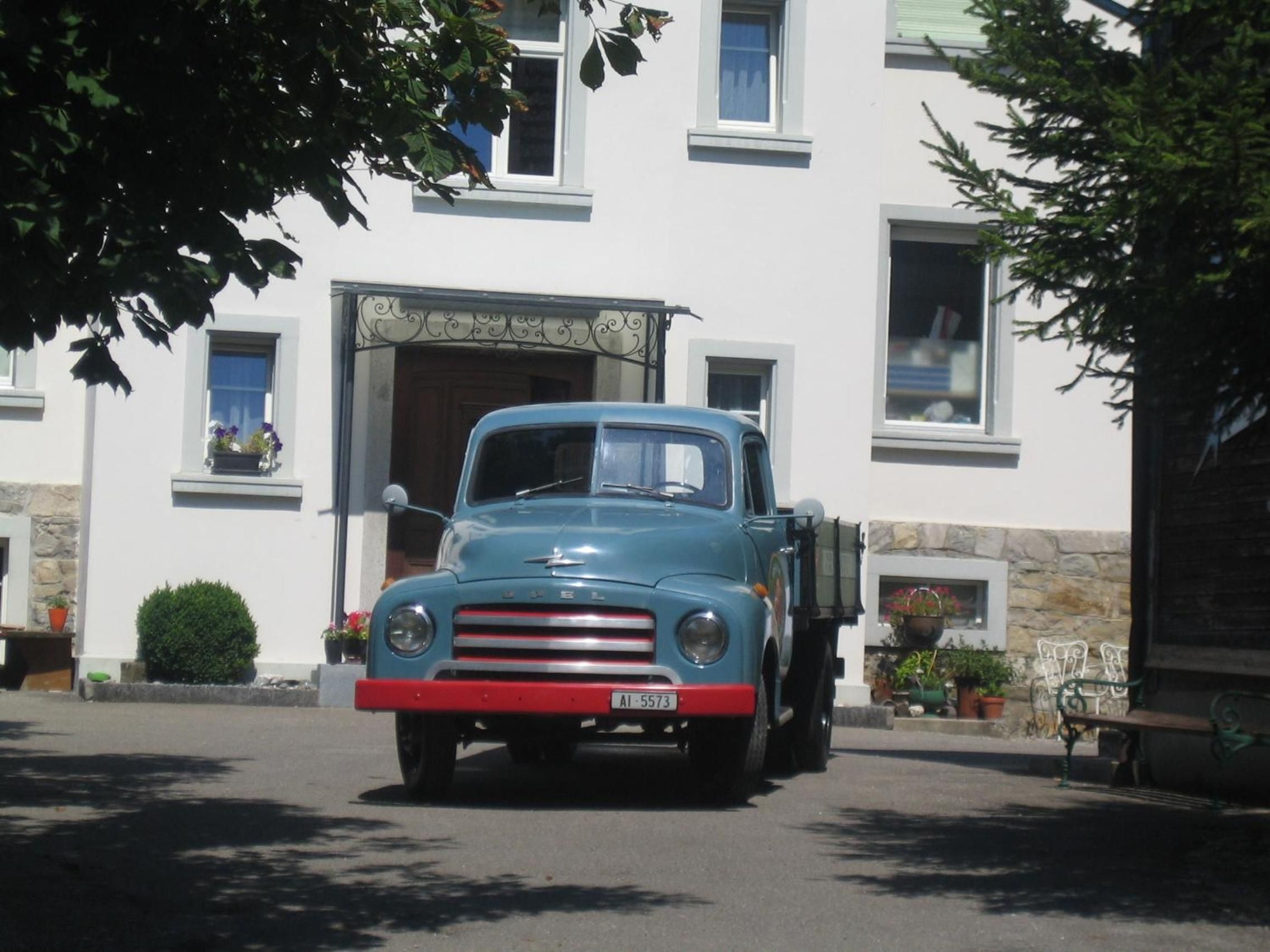 Un vecchio camioncino blu parcheggiato davanti a un edificio con facciata in pietra e numerose finestre.