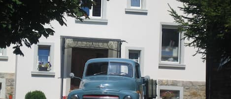 Un camión azul antiguo estacionado frente a un edificio de fachada de piedra y múltiples ventanas.