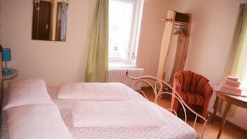 Una camera da letto con un letto, una sedia, un termosifone e una finestra con tende.