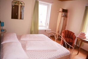 Quarto com cama, cadeira, radiador e janela com cortinas.