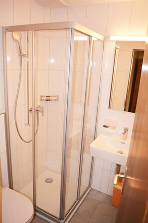 Un baño moderno con ducha de vidrio, lavamanos blanco y espejo sobre él.