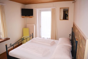 A hotel room with a bed, a television mounted on the wall, a chair, and a window with curtains.