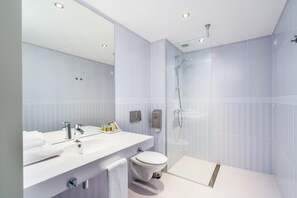 Een moderne badkamer met een douchecabine van glas, een wit wastafeltje met spiegel en een toilet.