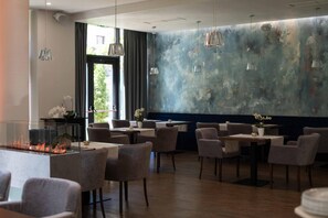 Een restaurant met een modern interieur, met een centraal openhaardelement, verschillende zithoeken en een grote abstracte muurschildering.