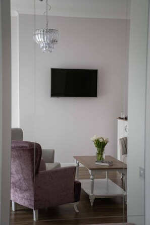 A modern living room with a flat-screen TV mounted on the wall, a dining table with a vase of flowers, and a purple armchair. - Impresamente Art Hotel (Sofia)