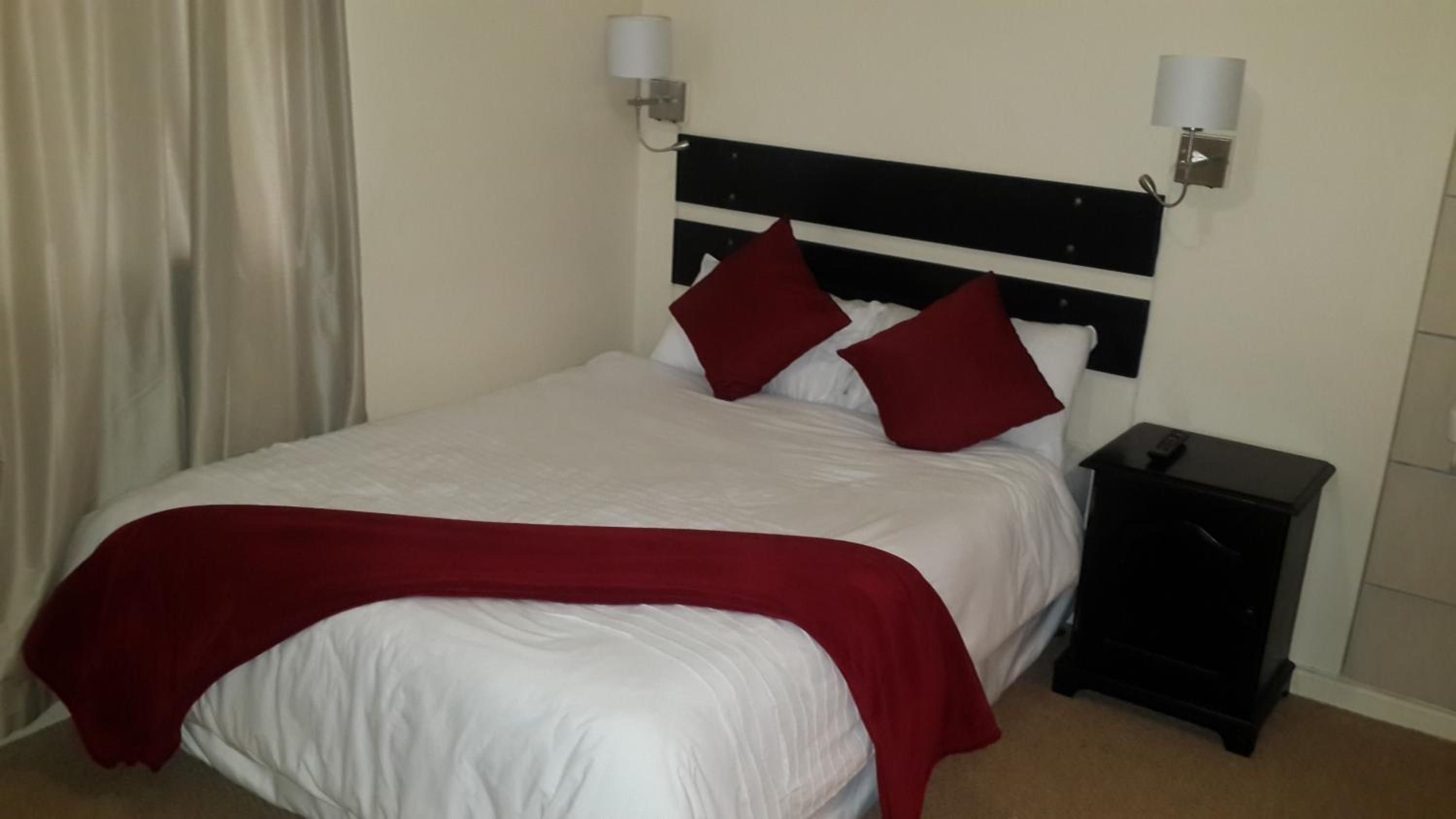 A hotel room with a bed, a nightstand, and a lamp.