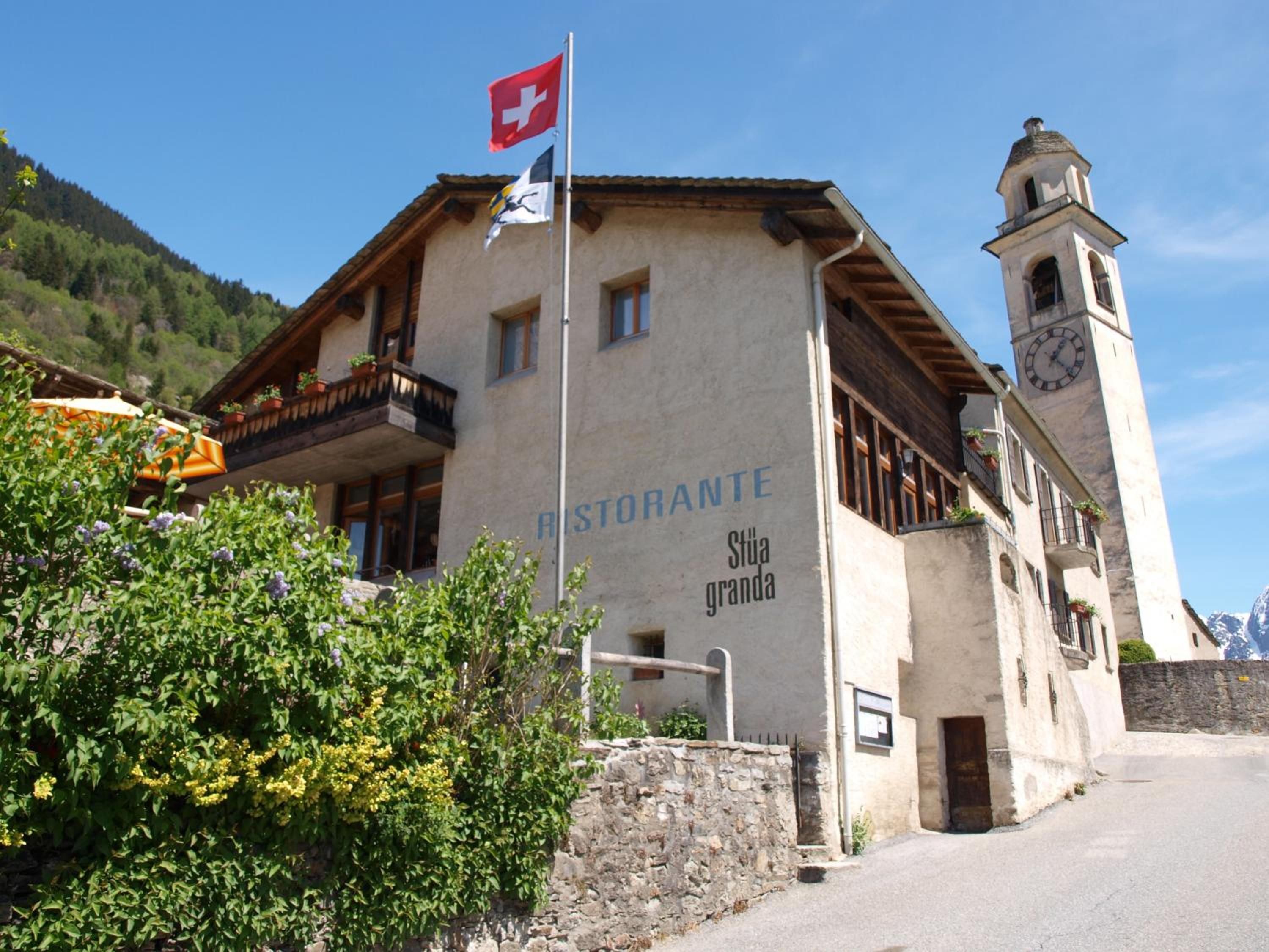 A building with a sign reading 'Ristorante Stia Granda,' a balcony, a clock tower, and a flag.