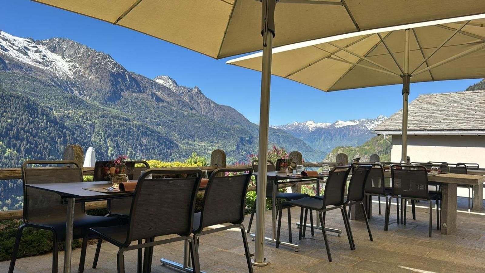 An outdoor dining area with tables and chairs, a large umbrella, and a mountain view.