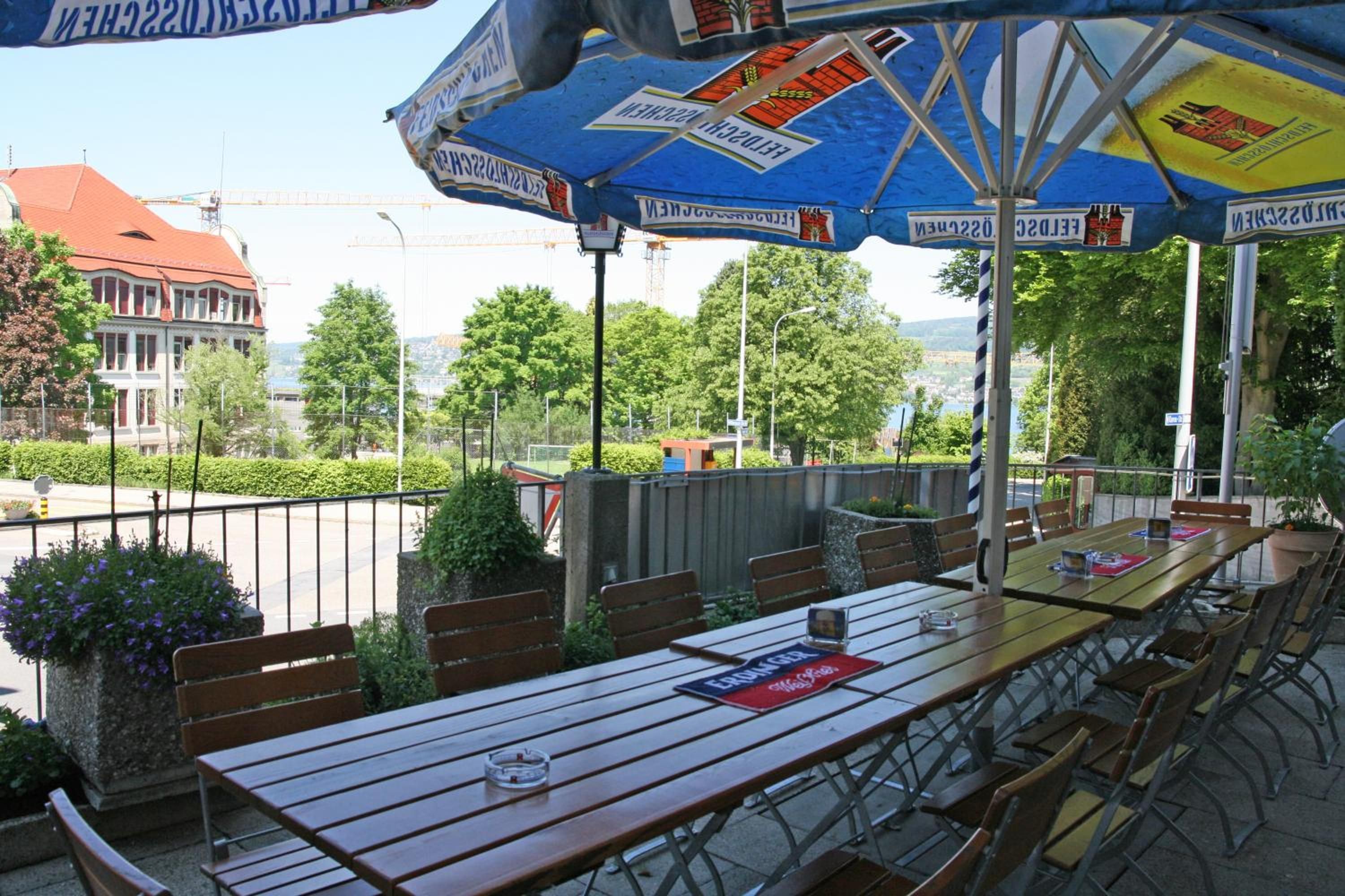 An outdoor seating area with tables and benches, overlooking a street with buildings and trees.