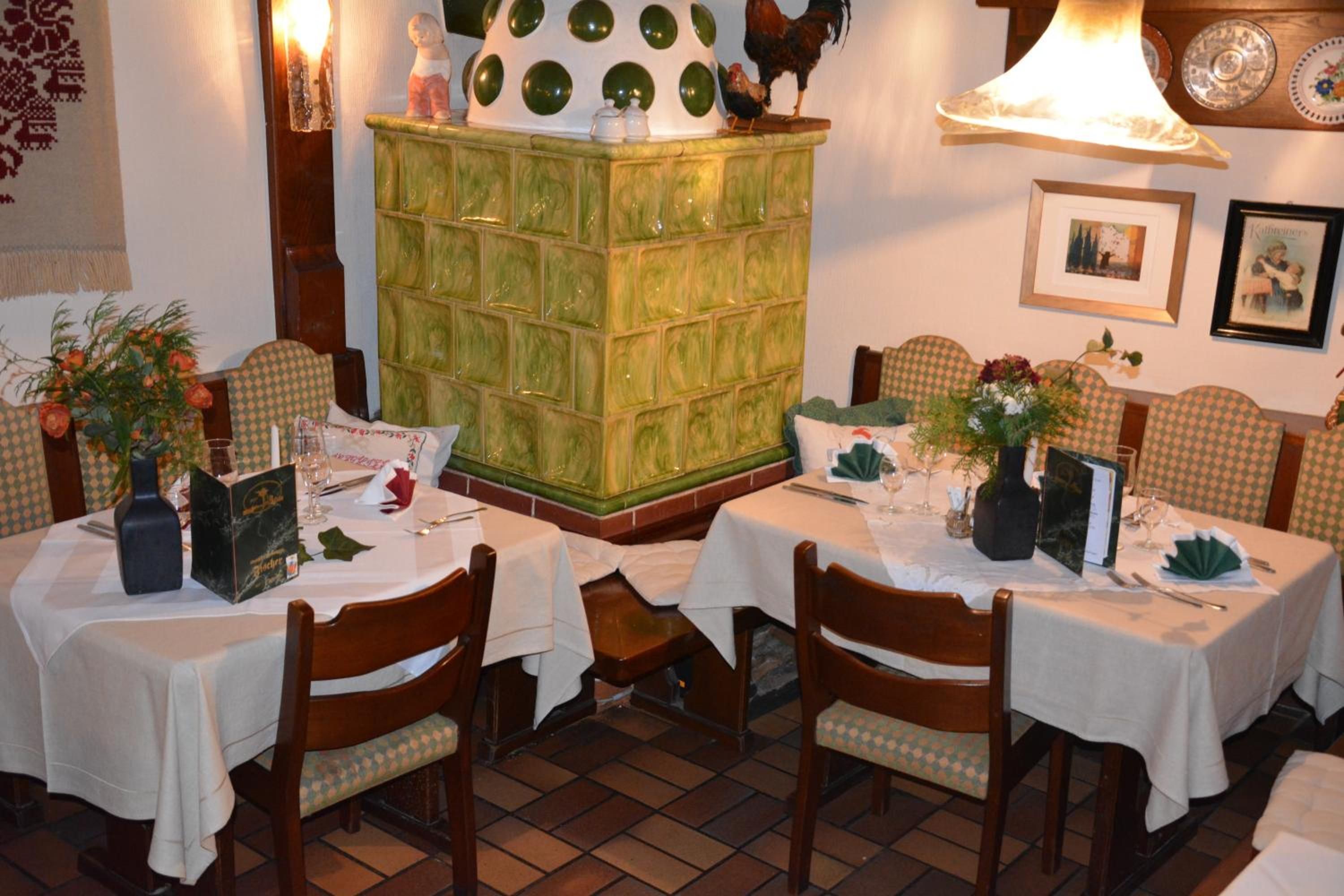 Un espace repas avec plusieurs tables prévues pour deux personnes, des chaises en bois et un séparateur en carreaux verts.