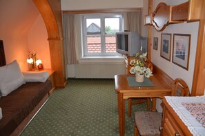 A hotel room with a bed, a small table with a vase of flowers, a television on a stand, and a window with curtains.