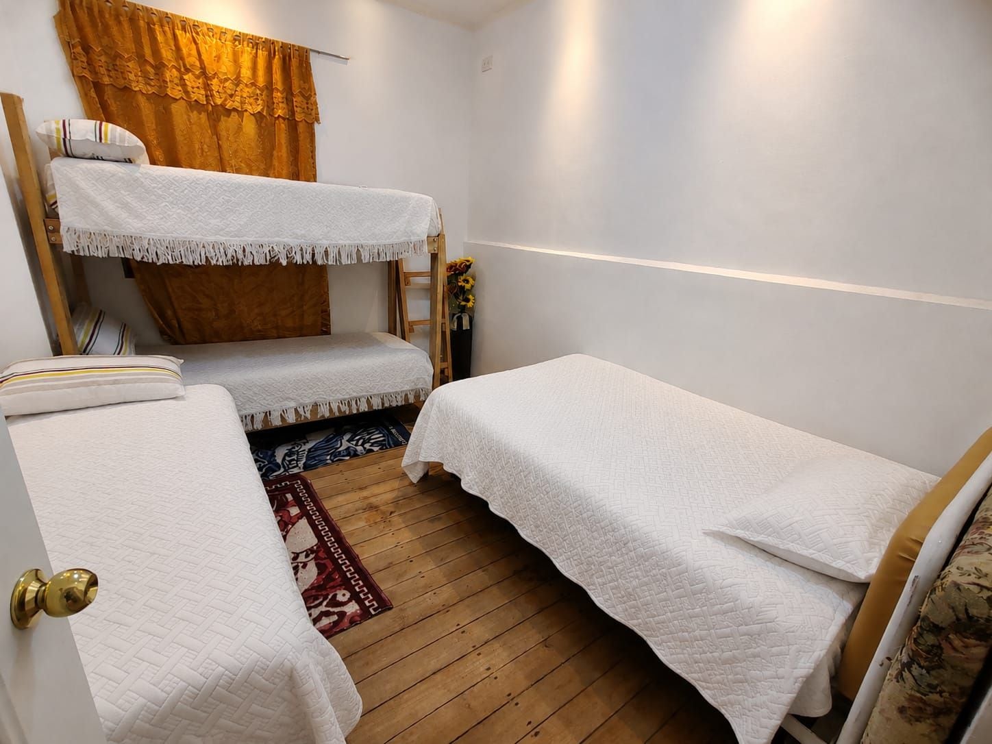 Una habitación con literas, piso de madera, alfombra estampada y una ventana con cortinas.