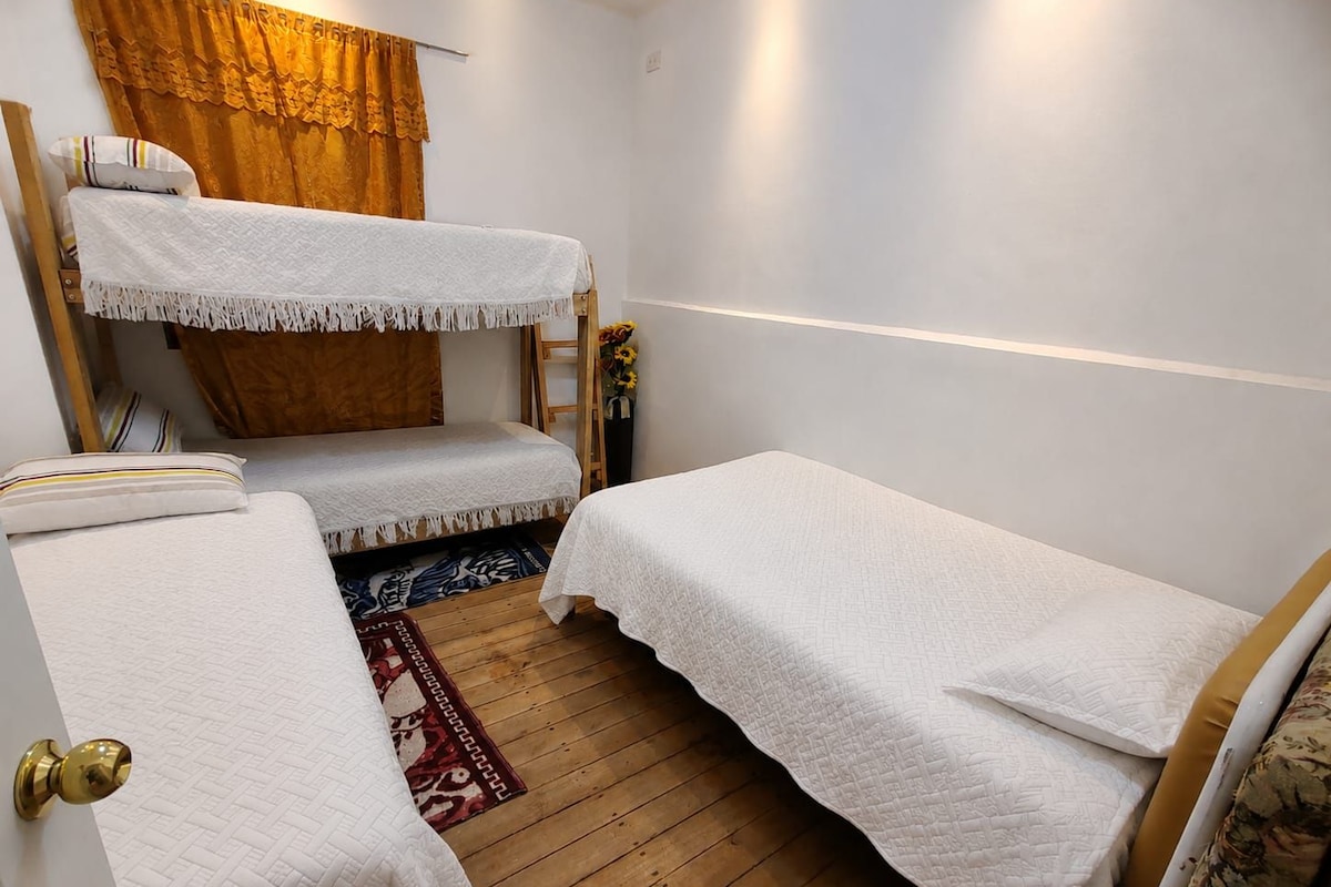 Ein Zimmer mit Etagenbetten, Holzboden, einem gemusterten Teppich und einem Fenster mit Vorhängen.