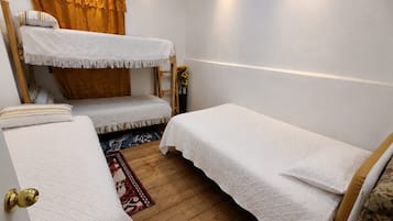 Una habitación con literas, piso de madera, alfombra estampada y una ventana con cortinas.