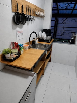 A modern kitchen with a wooden countertop, stainless steel sink, and a variety of cookware and utensils hanging above. - CUATRO ALTURAS EXPERIENCE (Quito)