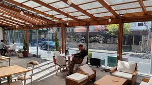 Ein Sitzbereich mit Tischen, Stühlen und einer Couch, mit Blick auf die Straße.