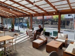 An indoor seating area with tables and chairs, a sofa, and a view of the street outside. - CUATRO ALTURAS EXPERIENCE (Quito)