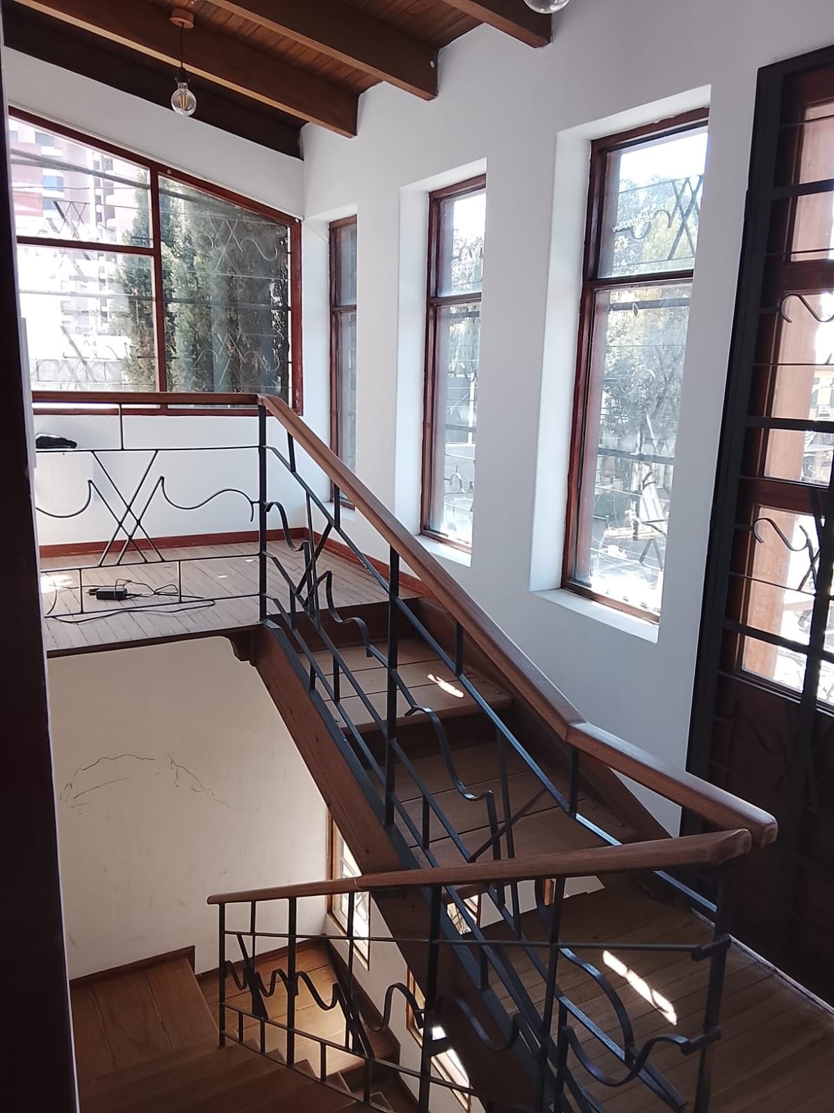 Una escalera con barandillas de metal que conduce a un piso superior, ventanas amplias con marcos de madera y vistas al exterior.