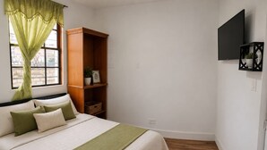 Ein Schlafzimmer mit einem Bett, einem Holzschrank, einem Fernseher und einem Fenster mit Vorhängen.