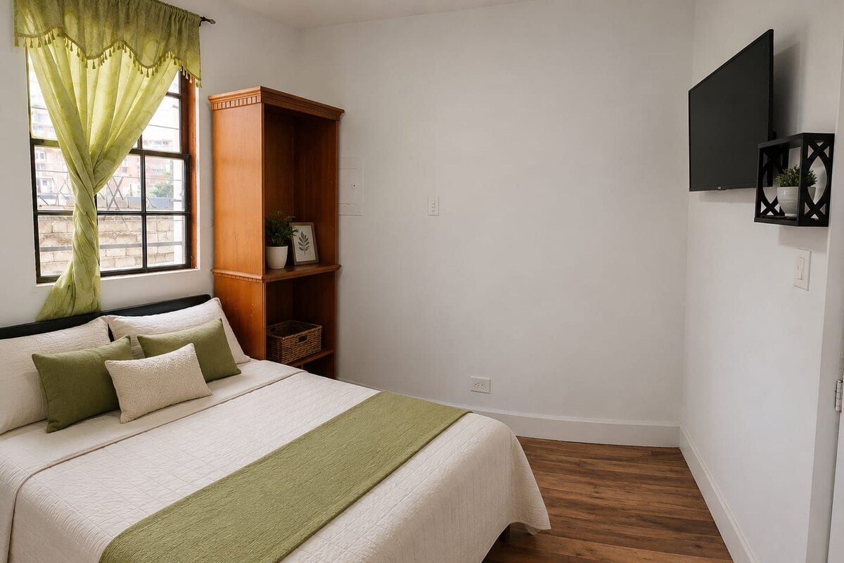 Ein Schlafzimmer mit einem Bett, einem Holzschrank, einem Fernseher und einem Fenster mit Vorhängen.
