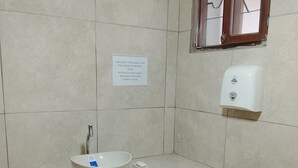 Ein Badezimmer mit Waschbecken, Seifenspender und einem Schild, das darauf hinweist, kein Papier in die Toilette zu werfen.