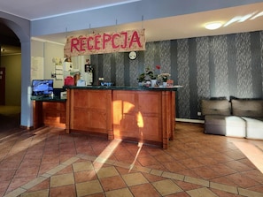 Un área de recepción con mostrador de madera, un reloj y un letrero que dice 'RECEPTJA'.