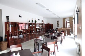 A restaurant with wooden tables and chairs, a wine rack with bottles, and a large window. - Hotel Corona (Kaplice)