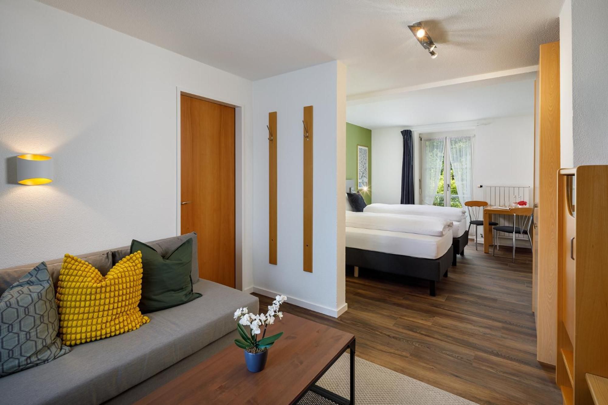 A hotel room with a sofa, a dining table, a bed, and a small balcony.