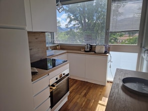 A modern kitchen with white cabinets, a black countertop, and a window with blinds.