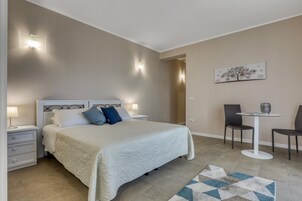 Un dormitorio con cama, mesitas de noche, un escritorio, dos sillas y una obra de arte en la pared.
