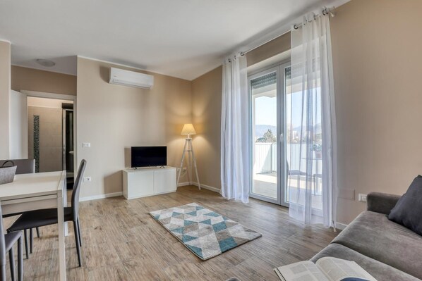 Una sala de estar moderna con un televisor de pantalla plana, una lámpara y vistas al exterior a través de amplios ventanales.