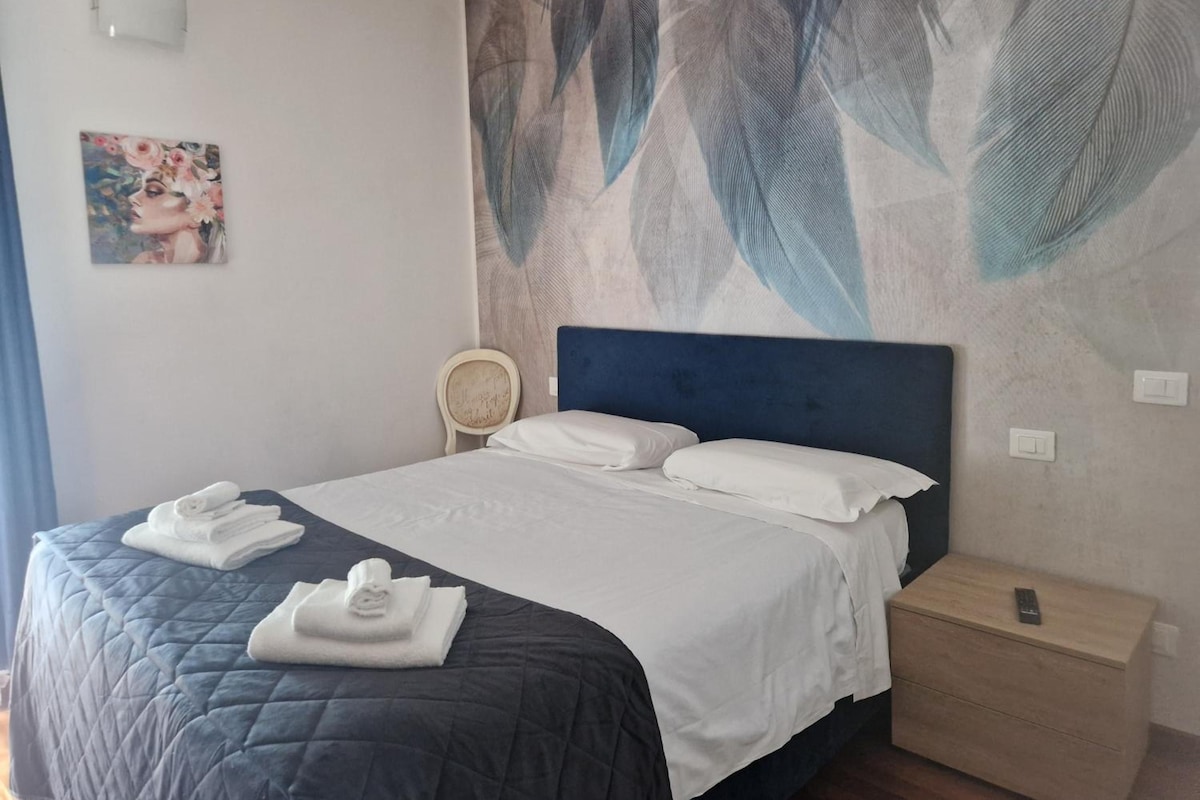 A hotel room with a bed, a nightstand, a chair, and a wall with a leaf pattern.