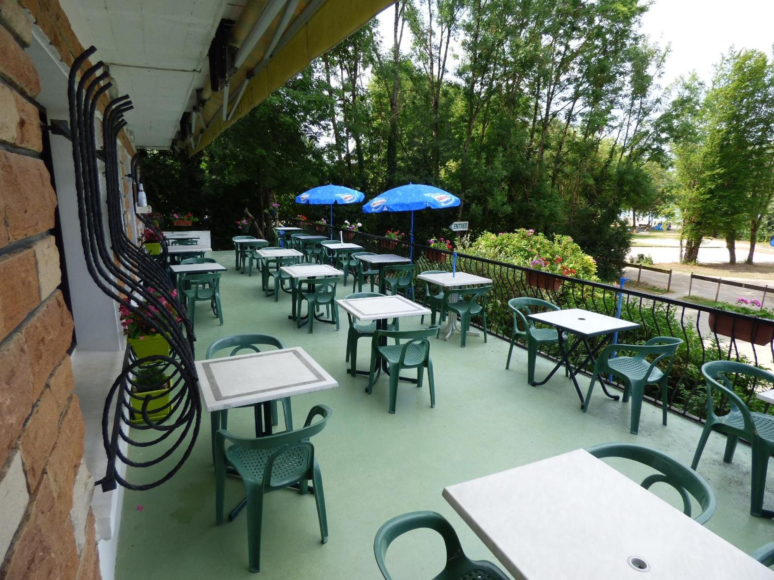 An outdoor patio with tables and chairs, some with umbrellas, and a brick wall on one side.