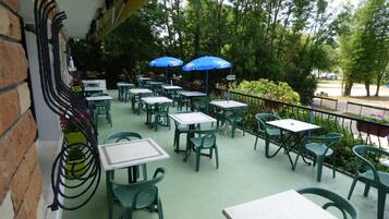 An outdoor patio with tables and chairs, some with umbrellas, and a brick wall on one side.