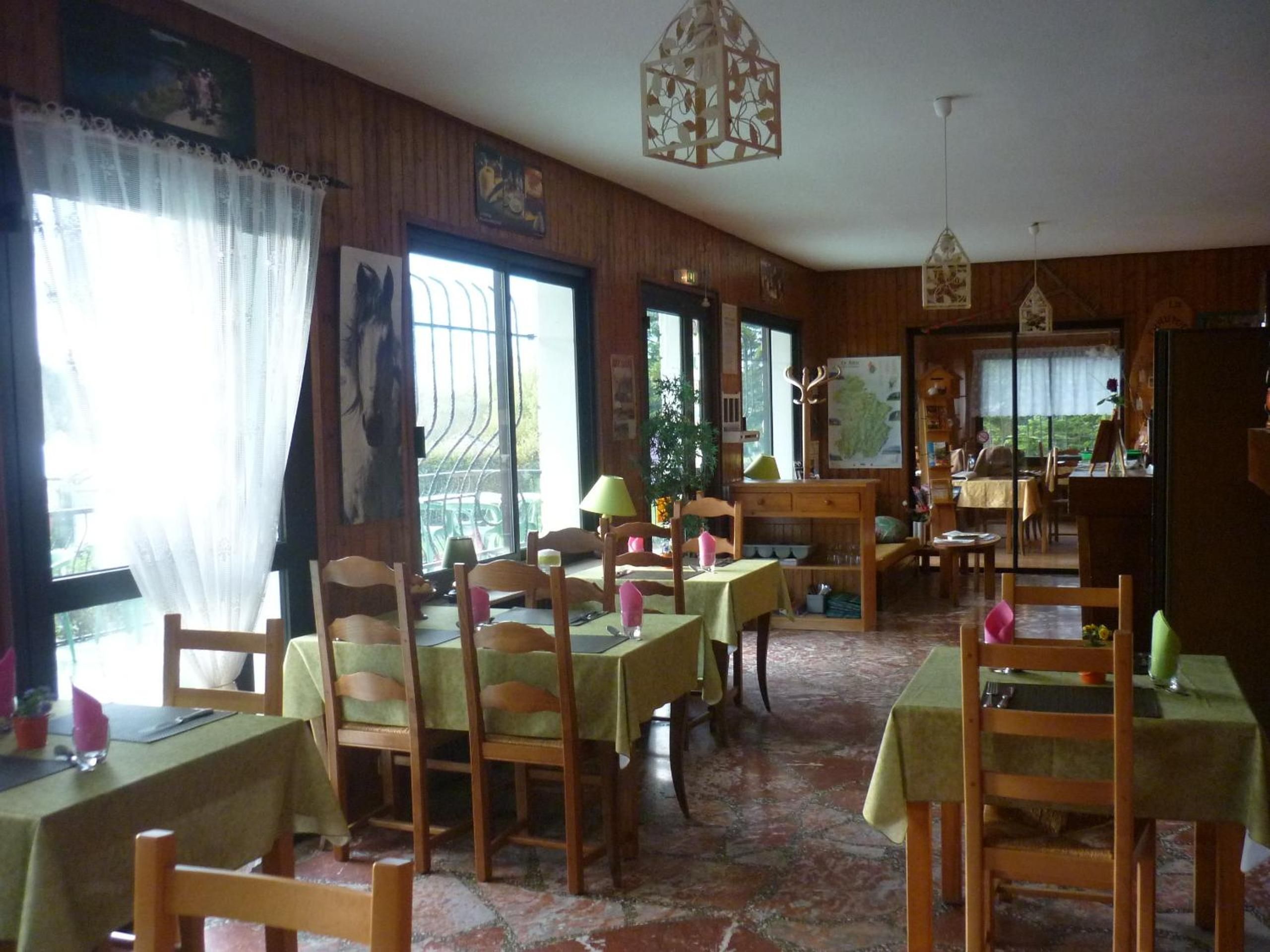 A dining area with wooden tables and chairs, large windows with curtains, and hanging light fixtures.