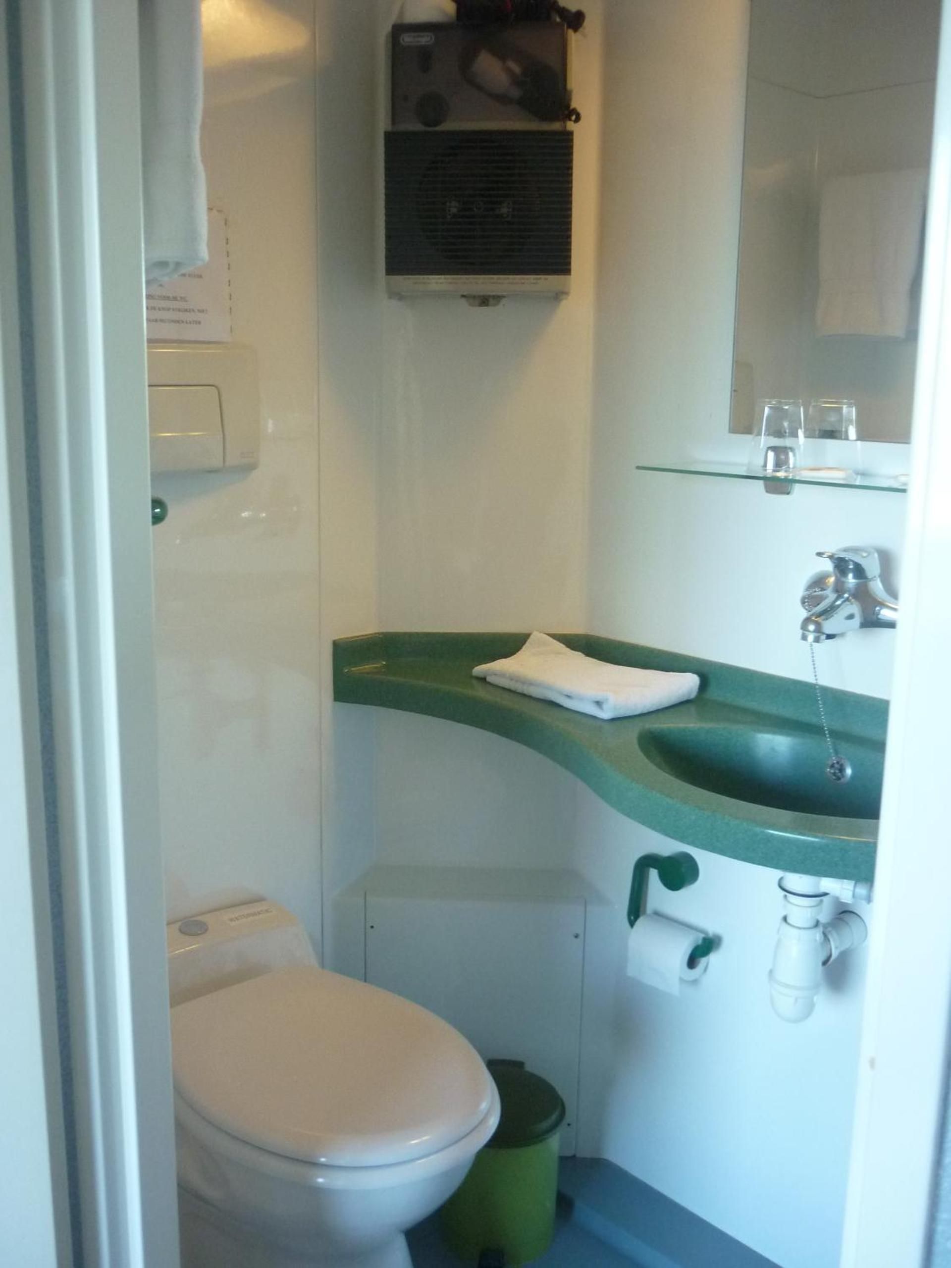 A compact bathroom with a white toilet, a green sink, and a mirror above the sink.