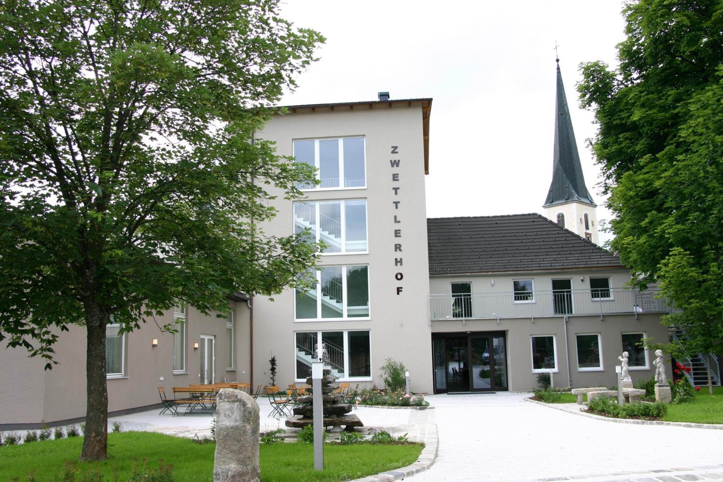 Un bâtiment sur lequel on peut lire l’inscription « ZWETTLERHOF », et une église avec un clocher en arrière-plan.