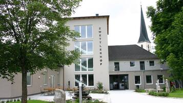 Un bâtiment sur lequel on peut lire l’inscription « ZWETTLERHOF », et une église avec un clocher en arrière-plan.