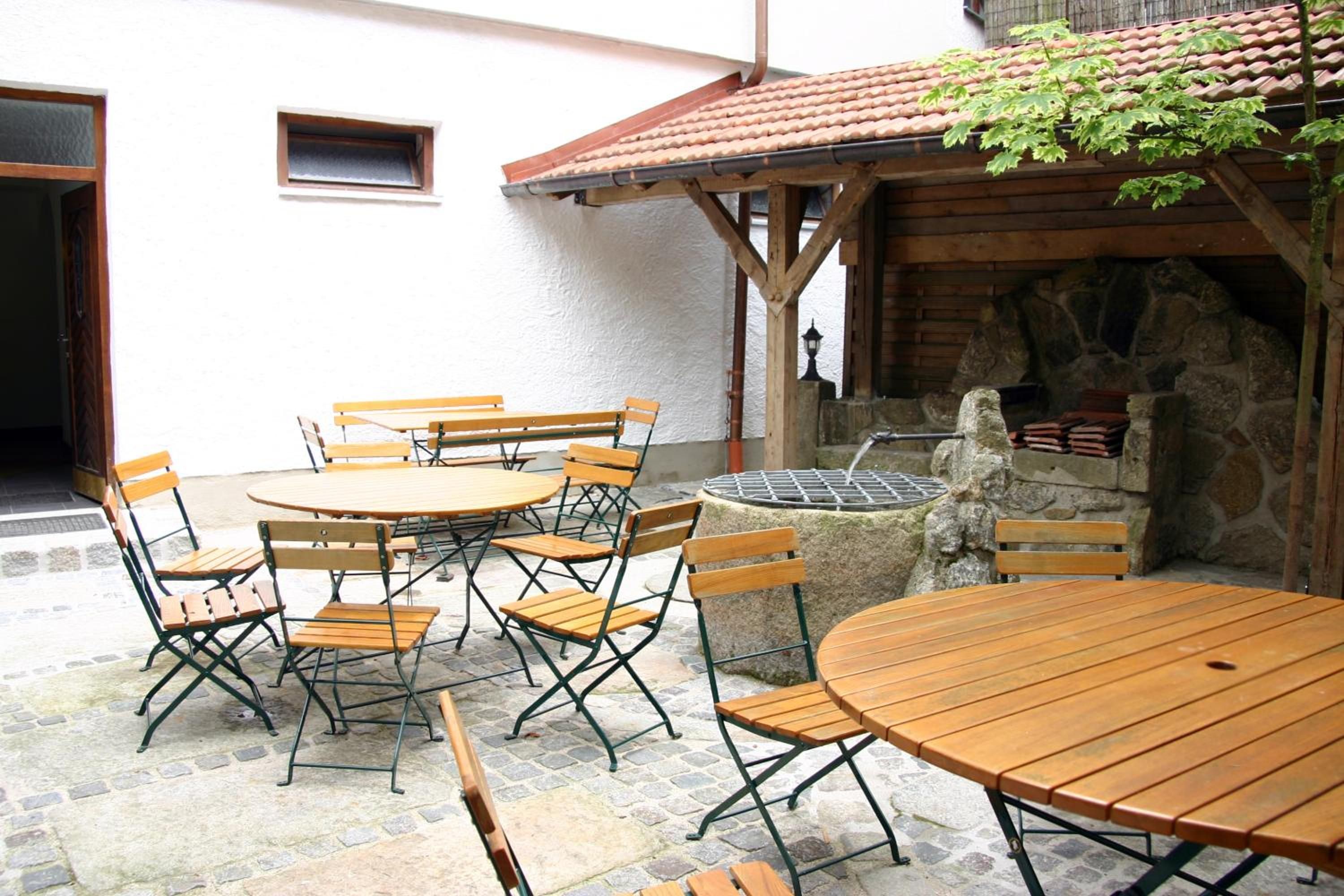 Eine Außenpatio mit Holztischen und -stühlen, einer Steinmauer und einem Ziegeldach.