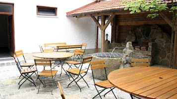Eine Außenpatio mit Holztischen und -stühlen, einer Steinmauer und einem Ziegeldach.