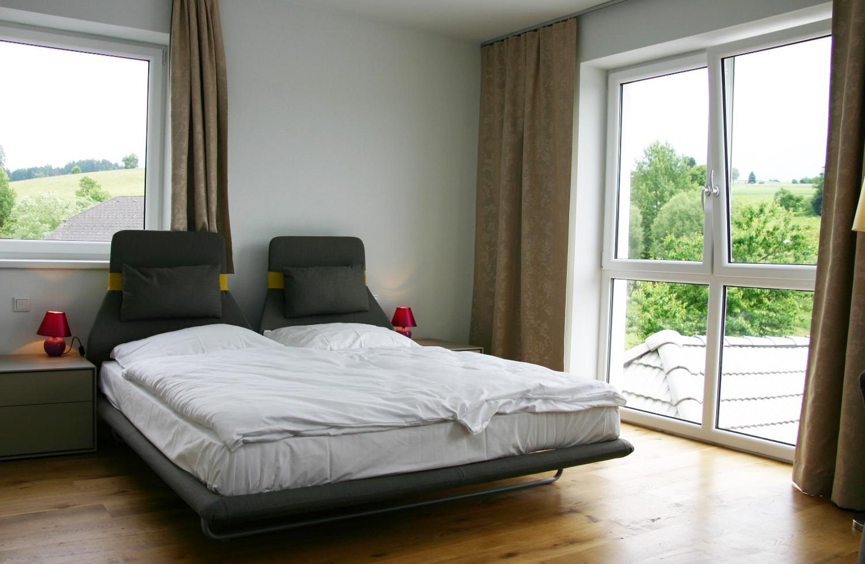 Une chambre à coucher avec un lit, deux tables de chevet, deux lampes et une grande fenêtre avec des rideaux.